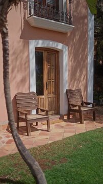 A mediterranean villa porch with wooden chairs, terracotta tiles, a palm tree, casting tranquil afternoon shadows.