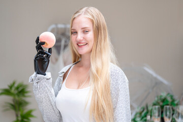 A young woman is using a robotic prosthetic arm attached to her body. She controls her hand to pick...