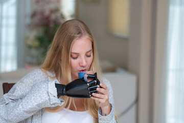 A young woman is using a robotic prosthetic arm attached to her body. She controls her hand to pick up objects glass coffee. The woman tries to control the smart arm in her home.