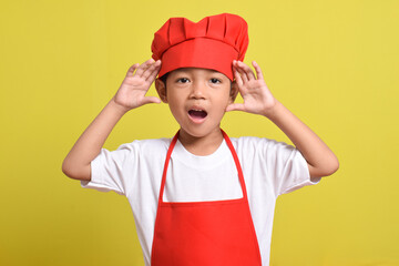 Cute little chef shouting sharing hot news about sale discount, hand near mouth isolated on yellow background. Asian boy wearing red apron and hat