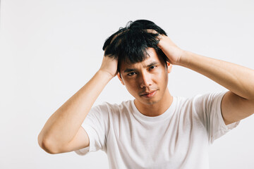 An Asian man, suffering from stress and a painful headache, holds his head with a sad and tired expression. Studio shot isolated on white background, showcasing his discomfort and illness.