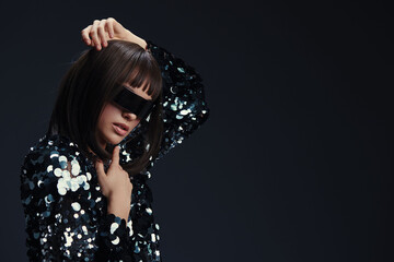 Woman in sequinned shirt and sunglasses posing confidently on dark background, embodying glamour...