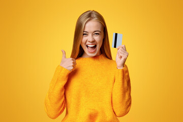 Father's credit card. Carefree young girl showing thumb up, excited about upcoming shopping