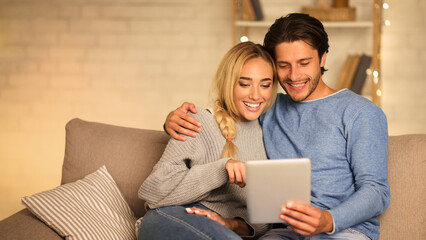 Loving spouses choosing film on tablet, resting together in cozy living room, free space