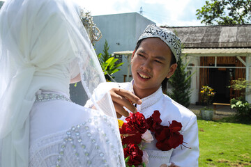 Young Indonesian Groom Holding Flowers Bouquet While Looking Bride On Park