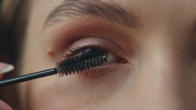 Green-eyed woman colouring eyelashes closeup. Unknown lady face applying mascara