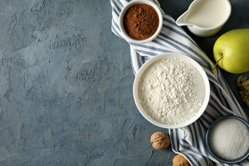 Ingredients for baking and apple on towel on gray background, space for text