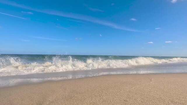 Camera tracks across sand into oncoming surf at Florida beach
