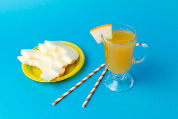 Fresh Honeydew Juice in Glass with Melon Slices on Yellow Plate Against Blue Background