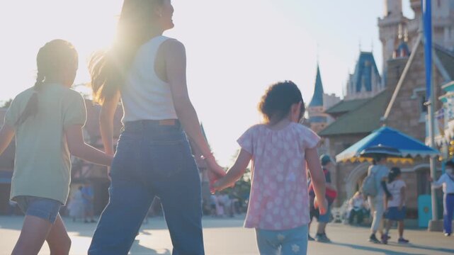 Asian mother and adorable kid daughters walking at the theme park.