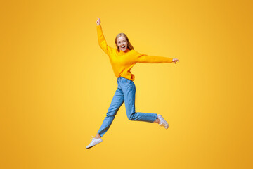 Jumping millennial girl in the air over orange studio background with free space
