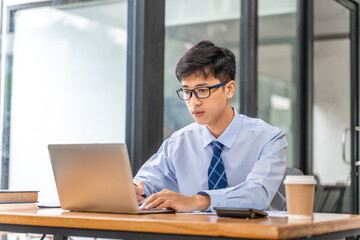 Young businessman working on his project in his office checking business result data from the printed sheets and his laptop computer