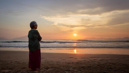 Fototapeta premium Older Asian woman staring looking at the sunset from the beach
