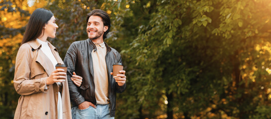 Cheerful man and woman drinking coffee and talking while dating in golden forest, copy space