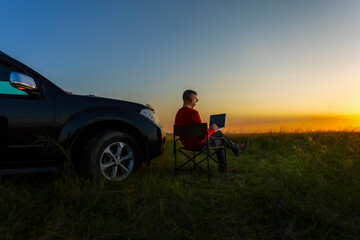 Naklejka premium Man using laptop while sitting at nature. Freelance work, remote work during vacation