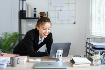 Fototapeta premium A businesswoman in a black suit is leaning over her desk, deeply focused on her work in a modern office environment