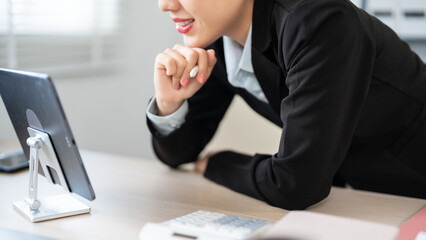 A businesswoman in a black suit is leaning over her desk, deeply focused on her work in a modern office environment