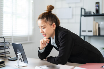A businesswoman in a black suit is leaning over her desk, deeply focused on her work in a modern...