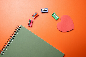 A notebook with a red heart on it and a pencil sharpener on top of it