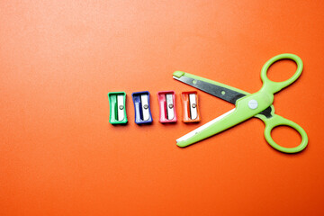 A pair of scissors is on a table with four different colored pencils