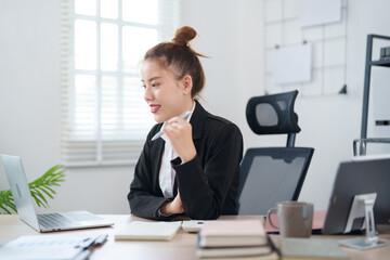 A confident businesswoman in a black suit is sitting at her desk, smiling as she engages in an online meeting, with notes and documents organized on the table in a modern office