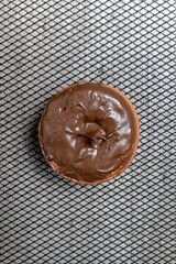 A chocolate mini donut sits on a metal mesh