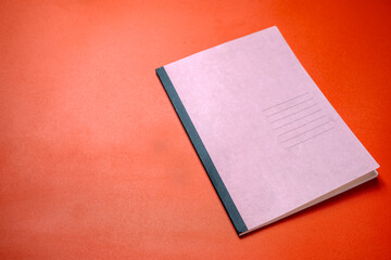 A pink notebook with a black spine sits on a red surface
