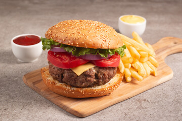 Homemade delicious hamburger with beef, onion, tomato, lettuce and cheese. Fresh burger close up on wooden rustic table with potato fries. Cheeseburger. Burger.