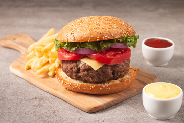 Homemade delicious hamburger with beef, onion, tomato, lettuce and cheese. Fresh burger close up on wooden rustic table with potato fries. Cheeseburger. Burger.