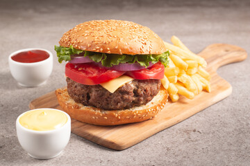 Homemade delicious hamburger with beef, onion, tomato, lettuce and cheese. Fresh burger close up on wooden rustic table with potato fries. Cheeseburger. Burger.