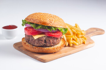 Homemade delicious hamburger with beef, onion, tomato, lettuce and cheese. Fresh burger close up on wooden rustic table with potato fries. Cheeseburger. Burger.