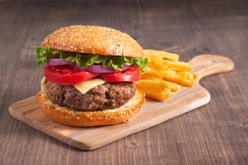 Homemade delicious hamburger with beef, onion, tomato, lettuce and cheese. Fresh burger close up on wooden rustic table with potato fries. Cheeseburger. Burger.