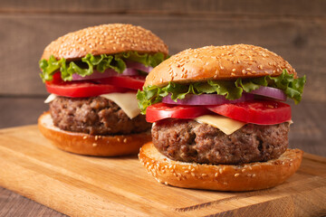 Homemade delicious hamburger with beef, onion, tomato, lettuce and cheese. Fresh burger close up on wooden rustic table with potato fries. Cheeseburger. Burger.