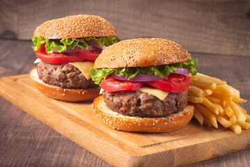 Homemade delicious hamburger with beef, onion, tomato, lettuce and cheese. Fresh burger close up on wooden rustic table with potato fries. Cheeseburger. Burger.
