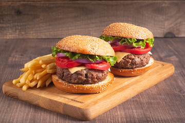 Homemade delicious hamburger with beef, onion, tomato, lettuce and cheese. Fresh burger close up on wooden rustic table with potato fries. Cheeseburger. Burger.