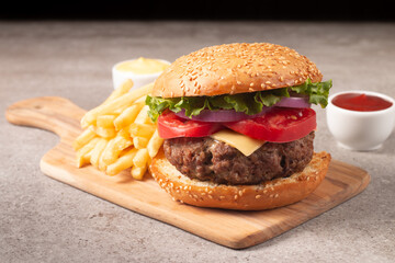 Homemade delicious hamburger with beef, onion, tomato, lettuce and cheese. Fresh burger close up on wooden rustic table with potato fries. Cheeseburger. Burger.