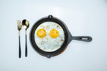 A plate of sunny side up eggs and a fork and knife on a white background