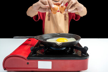 A young boy is cooking an sunny side up egg on a pan on a stove
