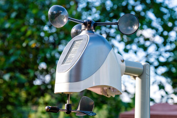 Individual weather station with a black wind vane is mounted on a pole in a garden. Personal meteorology and weather forecasting