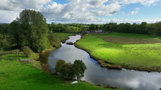 Finn River, County Monaghan, Ireland, September 2022. Drone pushes forward over bend in river soaring up across old bridge rising over pastures and grasslands on beautiful day.