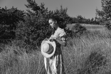 Woman in tall grass with hat nature and fashion fusion in black and white photo