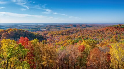 A scenic overlook of rolling hills covered in rich fall foliage, with trees in varying shades of red, orange, and yellow against a clear, blue sky