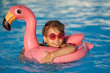 Cute funny toddler girl in a sunglasses relaxing on inflatable toy ring floating in pool have fun...