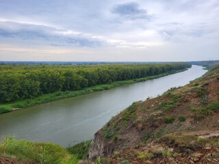Obraz premium A river viewed from a high mountain cliff. Behind is a forest, against the backdrop of a serene sky.