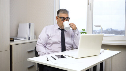 Businessman Drinking Tea and Working on Computer in Office