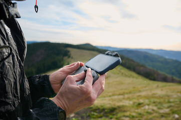 Close up view of drone operator holding remote controller in the mountains. Traveler controlling a drone flying over mountains with remote control. Shooting aerial videography and photography.