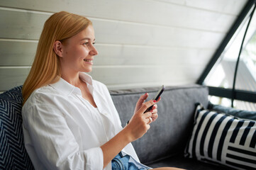 Fototapeta premium young pretty woman with blonde hair and a beautiful smile inside the room talking on a video call on a smartphone