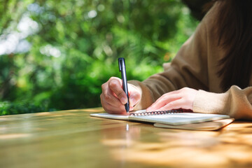Closeup image of a woman writing on a notebook in the outdoors