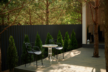 Obraz premium Country holiday in the nature. Country house territory chairs, table, wooden floor, surrounded by fir trees. Behind the territory is a pine forest.