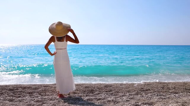 A woman in a white summer dress enjoys the turquoise sea of Mylos Beach at Lefkada island, Ionian Sea, Greece